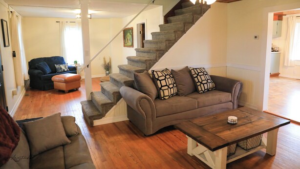 Un salon avec un escalier, un canapé, une table basse et un ventilateur de plafond.