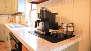 Une cuisine équipée d’une machine à café, d’un évier et d’un plan de travail surmonté d’un tapis noir et agrémenté d’un panier contenant des ustensiles de cuisine.
