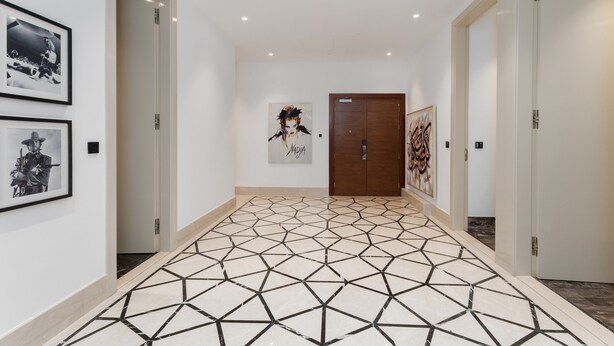 Een hal met een vloer met geometrisch patroon, zwart-wit foto’s in lijsten aan de wanden, en een deur met een 'MDIA' bordje.