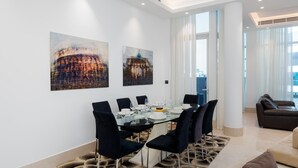 Een moderne eetruimte met een glazen tafel, zwarte stoelen en twee abstracte schilderijen aan de muur.