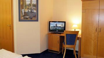 A hotel room with a bed, a desk with a television, a chair, and a wardrobe.