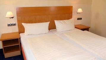 A double bed with two pillows, a wooden headboard, bedside lamps, a small shelf, and a painting on the wall.