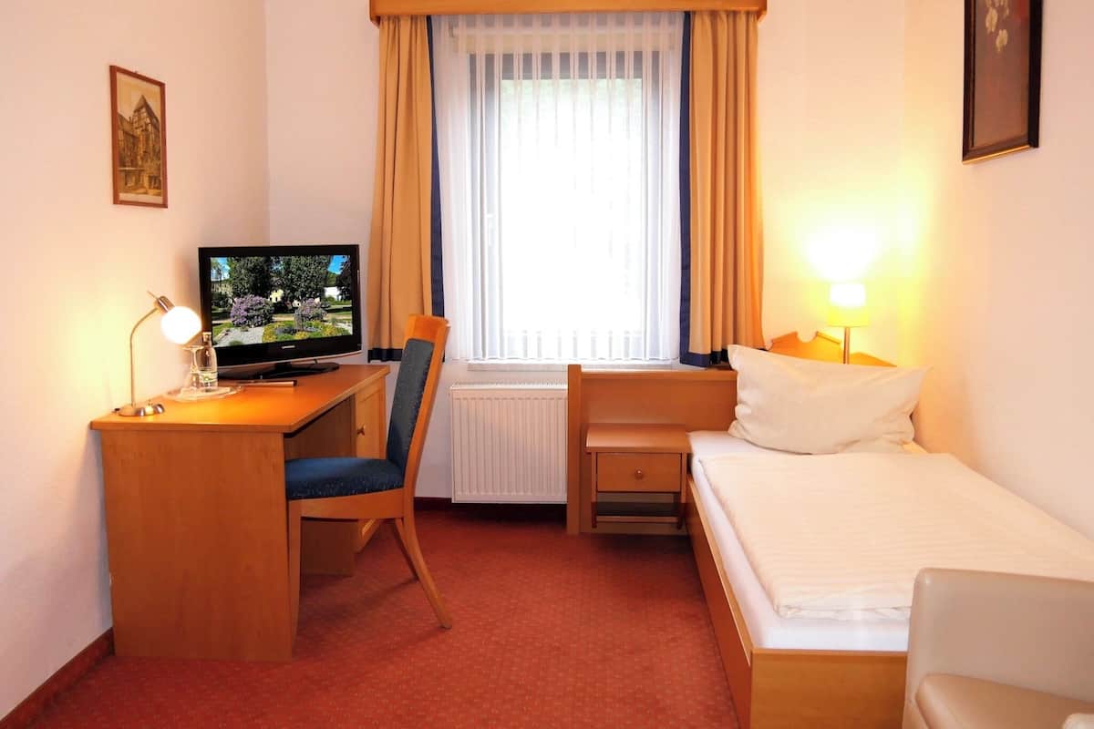 A hotel room with a bed, a desk with a chair, a television, and a window with curtains.