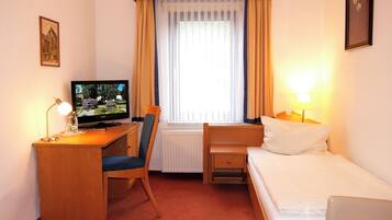 Een hotelkamer met een bed, een bureau met stoel, een televisie en een raam met gordijnen.