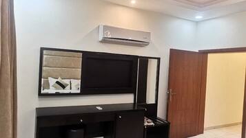 A room with a black desk, a mounted TV, a wall-mounted air conditioner, and a wooden door.