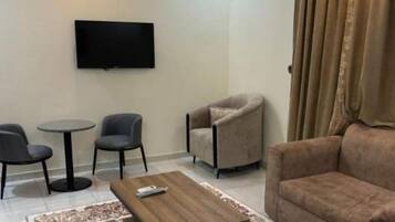 A living room with a brown sofa, a coffee table, two armchairs, a TV mounted on the wall, and a patterned rug.