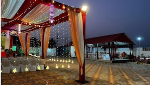 Un espacio para eventos al aire libre con alfombra estampada, cortinas drapeadas y luces colgantes.