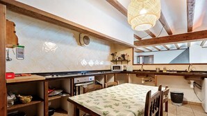 A kitchen with a dining table, wooden cabinets, a microwave, and a hanging light fixture. - Townhouse in Rojals (Montblanc)