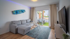 Een moderne woonkamer met een grijze modulaire bank, een flatscreen televisie, een blauw decoratief paneel en een schuifdeur die leidt naar een buitenruimte.