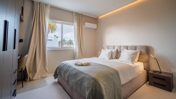 Een moderne slaapkamer met een groot bed, nachtkastjes, een kledingkast en een raam met gordijnen.