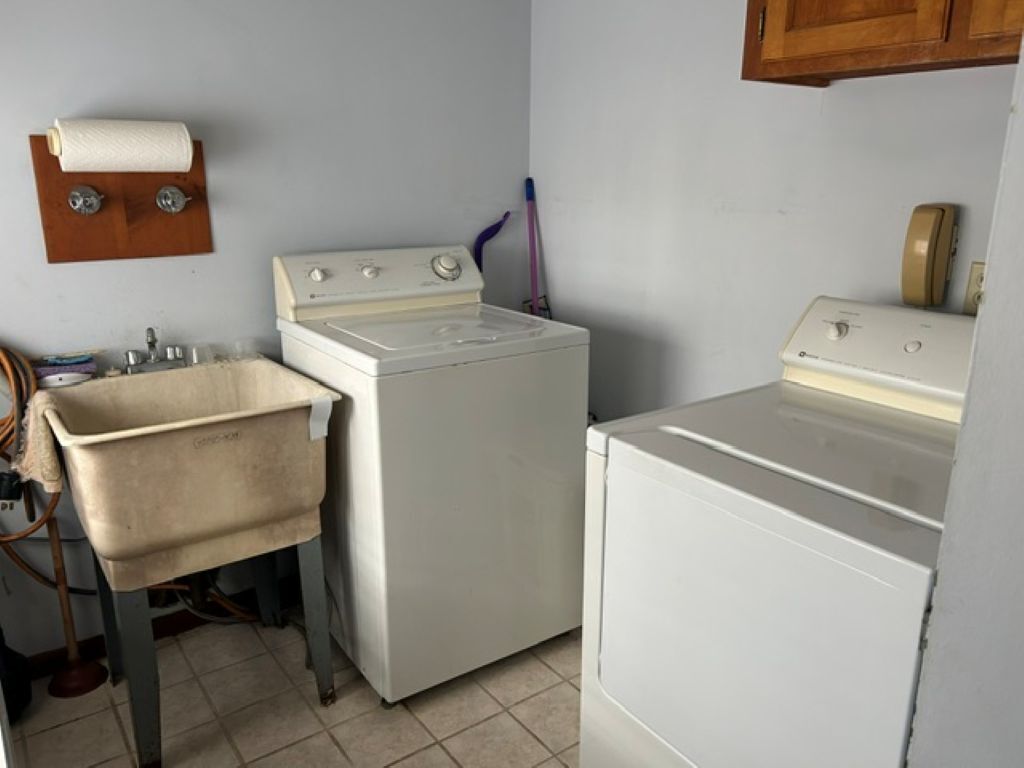 A laundry room with two white washing machines, a wooden towel rack, and a sink.