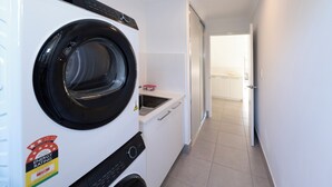 Un  área de lavandería compacta con lavadora y secadora de carga frontal, un lavamanos pequeño y una puerta que da a un baño.