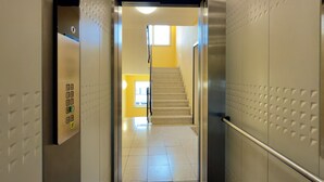 An elevator interior with a control panel, a handrail, and a view of a staircase leading to a yellow-lit area. - Ankerplatz-Neumarkt - My vacation apartment in the heart of Bremerhaven! (Bremerhaven)