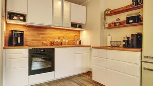 A modern kitchen with white cabinetry, a built-in oven, a coffee maker, and wooden countertops. - Ankerplatz-Neumarkt - My vacation apartment in the heart of Bremerhaven! (Bremerhaven)