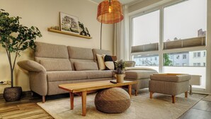 A modern living room with a sofa, ottoman, coffee table, and a large window. - Ankerplatz-Neumarkt - My vacation apartment in the heart of Bremerhaven! (Bremerhaven)