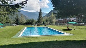 A rectangular swimming pool surrounded by grass, with a mountain backdrop and a few buildings in the distance. - Casa La Pica With Access to the Garden (Alins)