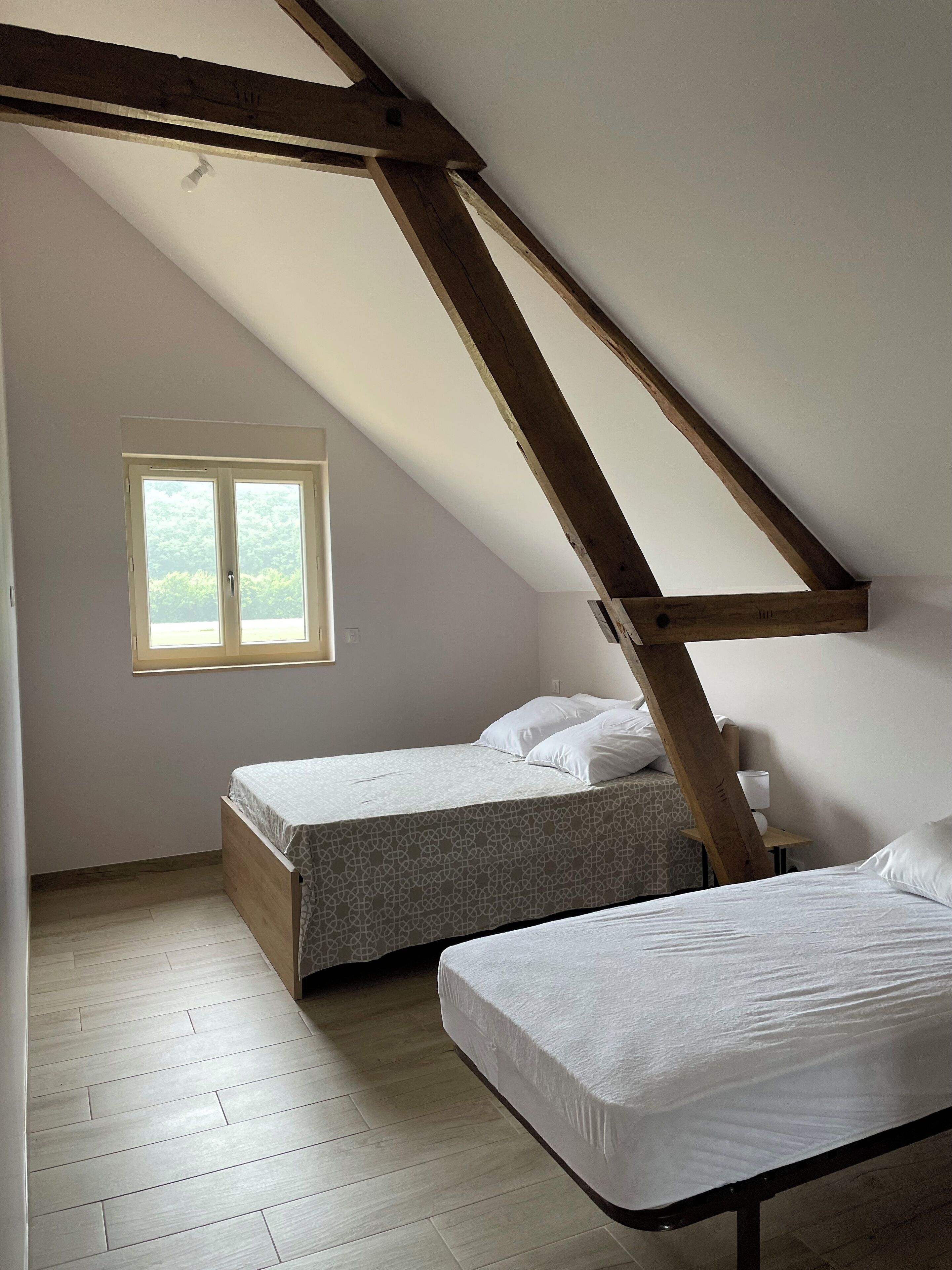 A small, well-lit attic bedroom with two beds, a window, and a sloped ceiling.