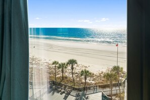 Blick auf einen Strand vom Balkon mit Geländer, Palmen und einer Flagge im Sand.