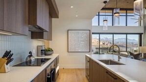 Una cocina moderna con armarios de madera, un lavamanos de acero inoxidable y un ventanal con vistas a la montaña.