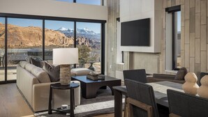 Una sala de estar moderna con un amplio ventanal que ofrece vistas a la montaña, un televisor de pantalla plana montado en la pared y una zona de estar acogedora con sofá y sillones.