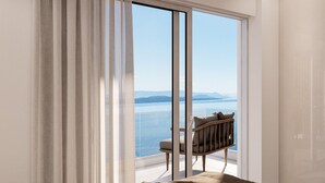 Ein modernes Zimmer mit einer großen Schiebeglasdoor, die auf einen Balkon mit Blick auf ein Gewässer und ferne Berge führt.