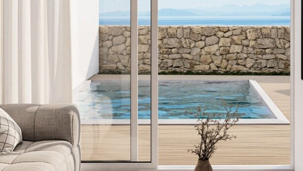 Ein modernes Interieur mit großem Fenster mit Blick auf einen Pool und eine Steinmauer, einer Couch und einer Vase mit Ästen.