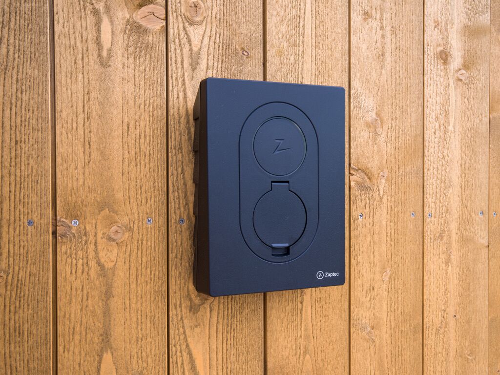 A black device with a circular button and a symbol, mounted on a wooden surface.