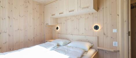 Een kamer met houten lambrisering, een bed, inbouwmeubels en wandlampen.