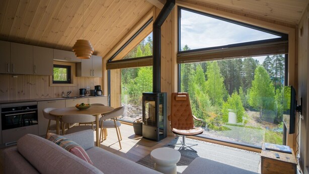 Ein gemütliches Blockhaus-Interieur mit Essbereich, Sofa und großem Fenster mit Blick auf den Wald.
