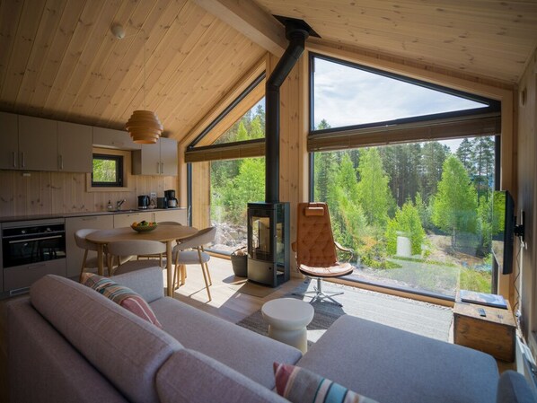 Ein gemütliches Blockhaus-Interieur mit Essbereich, Sofa und großem Fenster mit Blick auf den Wald.