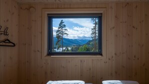 Ein Zimmer mit Holzwänden, einem Fenster mit Bergblick und zwei Betten.