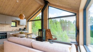 Ein modernes Interieur mit Holzbalkendecke, großen Fenstern, einer Couch, einem Esstisch und einer Küchenzeile.