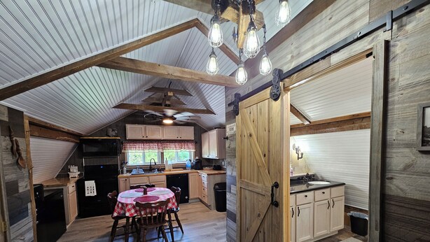 Une cuisine rustique avec des meubles en bois, une table à manger entourée de chaises et un plafond de style champêtre agrémenté de poutres apparentes et de luminaires suspendus.