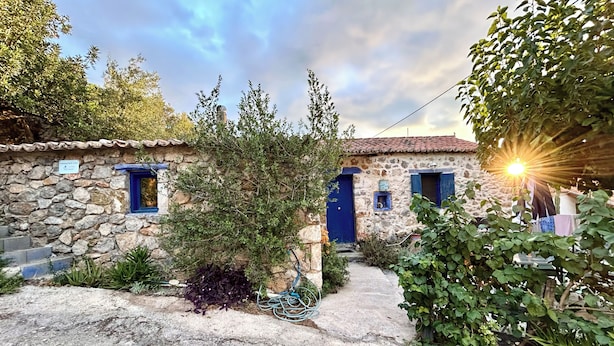 Un bâtiment en pierre avec un toit recouvert de tuiles, une porte bleue et une petite fenêtre.