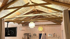 Une pièce rustique avec un haut plafond en bois, une table blanche, un lit à baldaquin et un téléviseur fixé au mur.