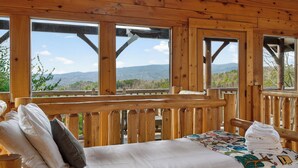 Une chambre dans un chalet en bois, avec un lit, des oreillers et une vue sur les montagnes.