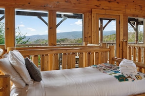 A wooden cabin room with a bed, pillows, and a view of mountains.