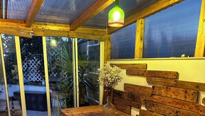 Une terrasse en bois avec une table et des bancs, un vase rempli de fleurs et un luminaire suspendu.
