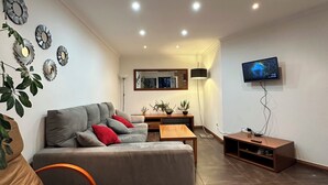 Un salon moderne avec un canapé gris, une table basse en bois et un téléviseur fixé au mur.