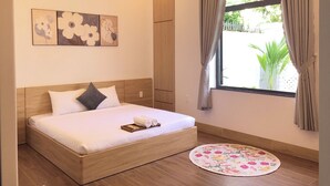 A neatly made bed with a wooden headboard, a round floral rug, and a window with curtains.