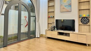 A modern living room with a large TV, wooden shelves, and a glass door with a red design.