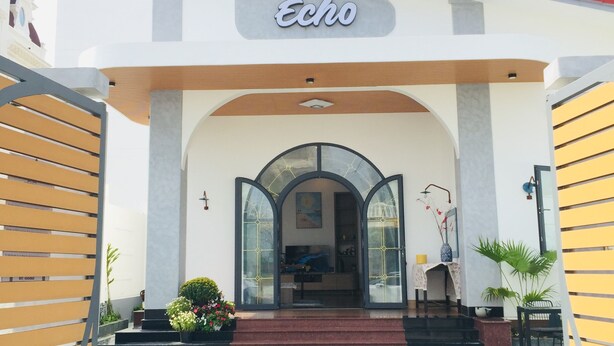 A hotel entrance with a sign reading "Echo," featuring a modern design with a red roof, a central archway, and a tiled entrance area.