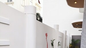 A modern indoor corridor with a tiled floor, potted plants, and a seating area with benches.