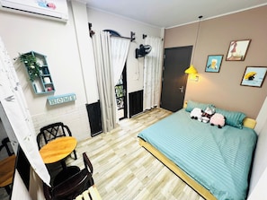 Une chambre à coucher comprenant un lit, un bureau, des chaises, une petite table, un ventilateur, une lampe et une porte.