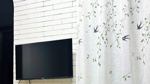 A room with a TV mounted on a white brick wall, a wooden table, a chair, and two plush toys. - ConiHouse III Thong Dong (Hue)