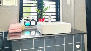 A bathroom with a black tiled countertop, a white sink, a mirror, a window with blinds, and a potted plant. - ConiHouse III Thong Dong (Hue)