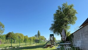 En græsplæne med gyngestativ, picnicbord og metalstole.