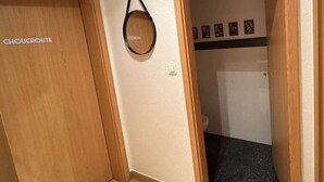 En gang med en trædør mærket 'CHOUCROUTE', en rund vægdekoration og en dør, der fører til et badeværelse med sort gulv.