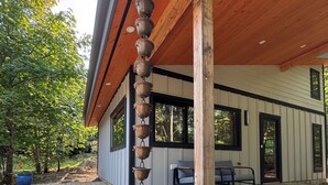 A wooden deck with a stone centerpiece, a modern building with a sloped roof, and a patio area with outdoor furniture. - Modern Farm Cottage on Private Acreage in Charming Point Roberts, WA (Point Roberts)