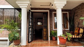 A covered entrance with a brick wall, white columns, and potted plants. - Artisanal Amazonian Suite, A Natural Refuge in Puyo (Puyo)